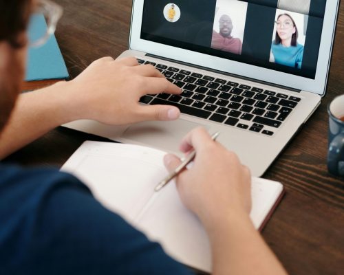 Person taking notes during a virtual meeting on a laptop screen with a diverse team.